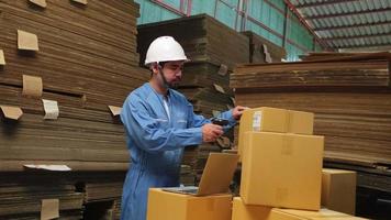 Asian male worker in safety uniform and hard hat using bar code scanner to check shipping orders at parcels warehouse, paper manufacture factory for the packing industry, logistic transport service. video