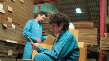 Two safety uniform workers and colleagues use laptop and mobile phone to check shipment orders stock at parcels warehouse, paper manufacture factory for packing industry, logistic transport service. video