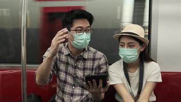 Young face mask couple Asian tourists search information, find travel locations by tablet map in a train cabin, passenger holiday trip lifestyle, casual transportation, journey vacation in Thailand.