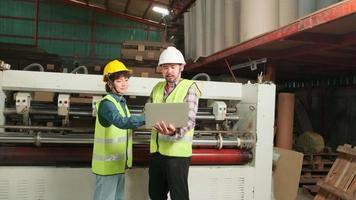 Safety uniform workers and industrial engineers with hardhat use laptop computer to check and control machines. Two professionals work in paper manufacturing factory, maintain production equipment. video