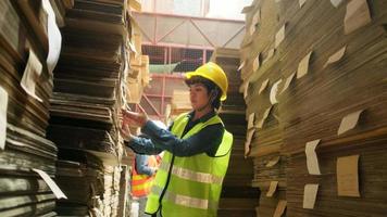 trabajadora con uniforme de seguridad y casco, la calidad del supervisor inspecciona el suministro de pedidos de existencias de embalaje en el almacén de almacenamiento de la fábrica, pilas de fabricación de papel apilado, industria de producción de reciclaje.