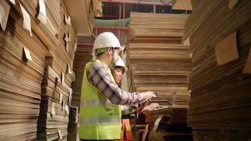 African American Female worker in a safety uniform and hard hat and male colleague inspect storage, stock order at factory warehouse, piles of stacking paper manufacture, industry product management. video