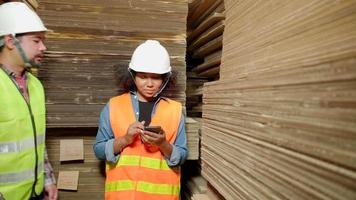 Warehouse female worker in safety uniform mobile phone addicts works idle, male manager orders to check supply stocks in industrial factory, piles of stacking paper manufacture, product distribution.