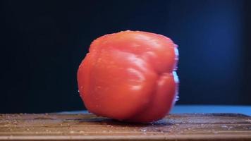 Ripe red bell pepper with thick peduncle rotates shaking small water drops on brown wooden board slow motion extreme closeup