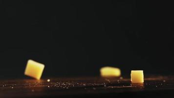 pedaços de queijo duro fresco de delicatessen com migalhas caem sobre a mesa escura no fundo preto macro visão câmera lenta video