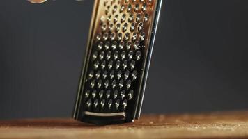 Chef in gloves grates delicious hard cheese lump for pasta with hand grater on wooden board extreme close view slow motion video