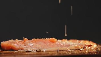 Pouring sea salt on slice of delicious red fish to cook delicatessen course on black background extreme closeup slow motion video