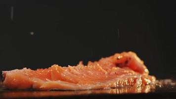 verser du sel sur le filet de délicieux poisson rouge pour cuisiner un cours spécial à bord sur fond noir extrême gros plan ralenti