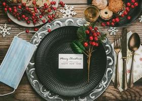 fondo del concepto de navidad cena de navidad con máscara médica, cubiertos antiguos vintage y diferentes platos de comida en la mesa de madera foto