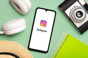 Instagram application icon on white screen of smartphone with white wireless headphone,vintage photo camera,hat and notebook