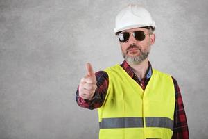 Man construction worker in White helmet and sunglasses is showing thumbs up photo