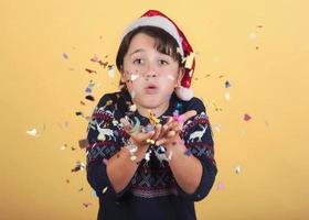 niño soplando confeti con sombrero de santa claus de navidad foto