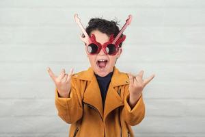 niño con gafas de sol haciendo símbolo de roca con las manos arriba foto