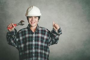 smiling boy with a white helmet and holding a wrench photo