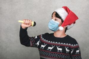 feliz navidad, niño con máscara médica cantando villancicos con un micrófono foto