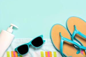 Summer holiday concept.Top view of blue flip flops,beach towel, blue sunglasses and bottle of sunscreen with copy space photo