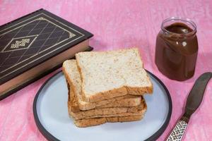 Whole wheat bread loaf slice has chocolate on pink table. photo