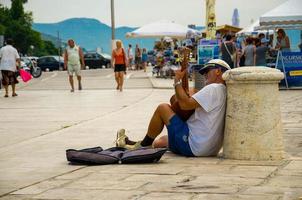 músico callejero con guitarra y gorra de marinero está sentado en la calle en la ciudad portuaria foto