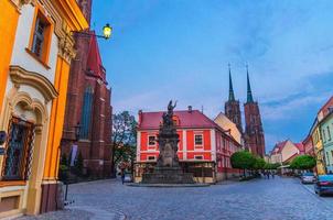 Monument on square, cobblestone road street with green trees, Cathedral of St. John the Baptist photo