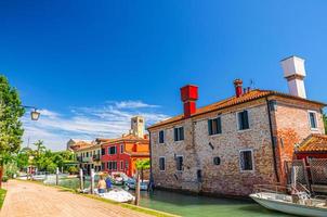 Torcello island with embankment promenade along water canal with motor boats and colorful buildings photo