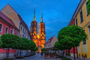 Street with cobblestone road, green trees, colorful buildings, Cathedral of St. John the Baptist church photo