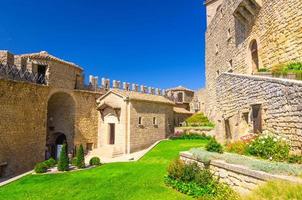 Courtyard with green grass lawn of Prima Torre Guaita first medieval tower with stone brick fortress wall photo