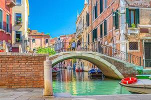 puente a través del estrecho canal de agua en venecia con barcos amarrados entre viejos edificios coloridos foto