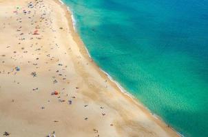 Top aerial view of sandy beach with people tourists sunbathing and Atlantic Ocean azure turquoise water, Praia da Nazare photo