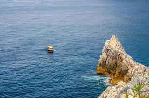 Yellow boat on blue dark water of Grotta di Lord Byron near coast with rock cliff, Portovenere town photo