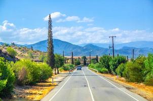 paisaje de chipre con vehículos de automóviles que recorren la carretera asfaltada en el valle con campos secos amarillos, cipreses foto