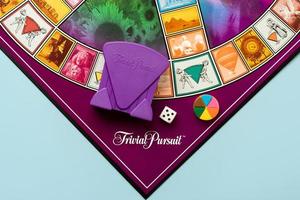 juego de mesa de búsqueda trivial con dado blanco, piezas de plástico de colores y tarjetero morado foto