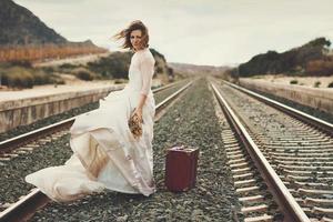 novia pensativa con una maleta roja en las vías del tren