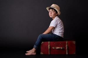 niño pensativo sentado en una maleta foto