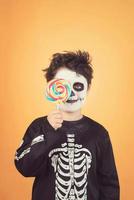 feliz halloween niño divertido en un disfraz de esqueleto que cubre el ojo con piruleta foto