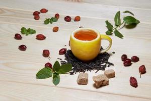 cup of tea with hip roses, on wooden table. A cup made of real lemon photo
