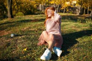 Portraits of a charming red-haired girl with a cute face. Girl posing in autumn park in a sweater and a coral-colored skirt. The girl has a wonderful mood photo