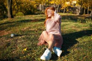 retratos de una encantadora chica pelirroja con una cara linda. chica posando en el parque de otoño con un suéter y una falda de color coral. la niña tiene un estado de ánimo maravilloso foto