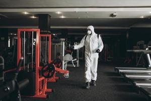 limpieza y desinfección en lugares concurridos en medio de la epidemia de coronavirus limpieza y desinfección de gimnasios prevención de infecciones y control de epidemias. traje de protección y máscara y bolsa de spray foto