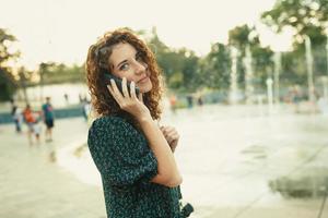 Portraits of a charming red-haired girl with a pretty face. The girl talks cutely with someone on the phone. She has a great mood and a sweet smile photo