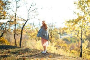 retratos de una encantadora chica pelirroja con una cara linda. chica posando en el parque de otoño con un suéter y una falda de color coral. la niña tiene un estado de ánimo maravilloso foto