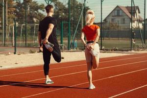 girl and a guy doing a warm-up before sports exercises at the school stadium photo