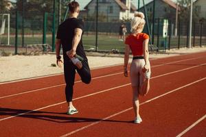 girl and a guy doing a warm-up before sports exercises at the school stadium photo