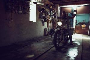 un hombre brutal y guapo con barba sentado en una motocicleta en su garaje foto
