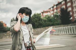 mujer con máscara médica con una cámara mira un mapa de la ciudad foto