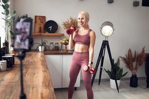 young beautiful blonde takes care of her body while at home during quarantine. She trains people online through her mobile phone photo