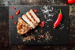 pork cooked in a pan and cut into pieces with spices on a dark stone background photo