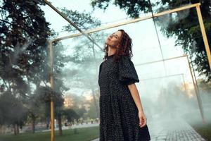 cute red-haired curly girl rejoices under the water fogger in the city center photo