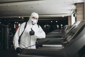 Cleaning and Disinfection in crowded places amid the coronavirus epidemic Gym cleaning and disinfection Infection prevention and control of epidemic. Protective suit and mask and spray bag photo