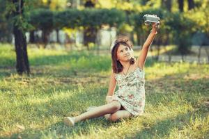 little girl is played by photo camera sitting on grass in park. Doing Selfie and photographing the world around