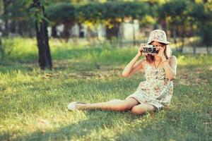 little girl is played by photo camera sitting on grass in park. Doing Selfie and photographing the world around